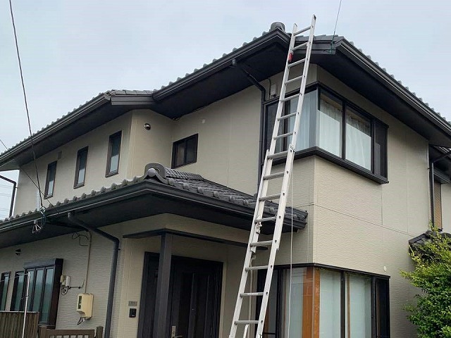 雨漏り調査を行うために屋根はしごをかけている住宅の全景