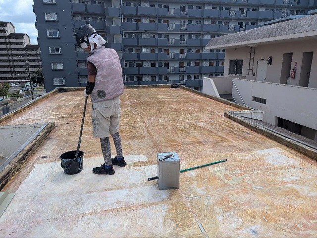 施設建物の屋上防水メンテナンスで床面にプライマーを塗布する職人