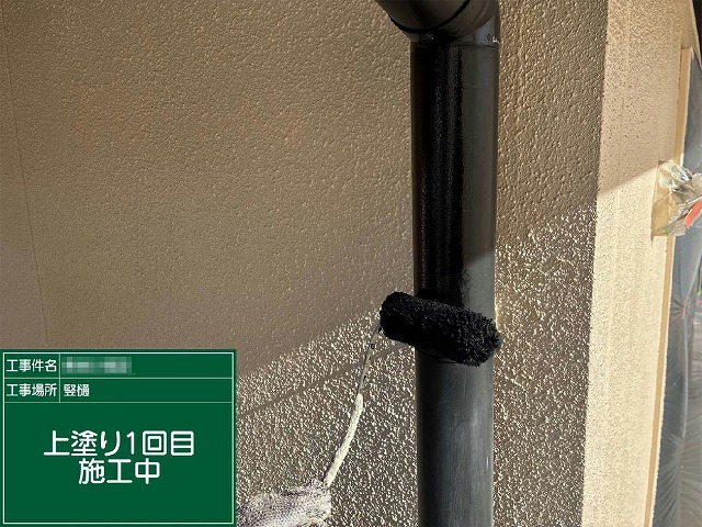 縦樋にローラーで上塗り1回目を施工している様子