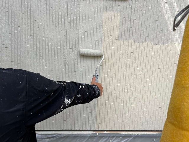 外壁サイディングに白系の色の塗料で塗装を行う塗装工