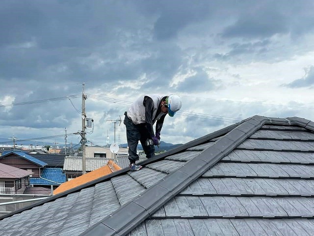 漆喰工事で屋根の上で棟瓦をビスで固定している屋根職人