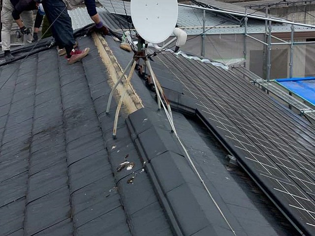 屋根の上で棟瓦を取り外す屋根職人