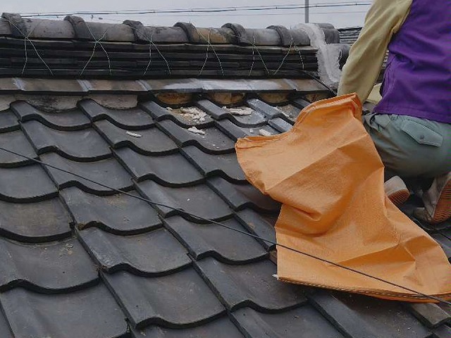 漆喰詰め直し工事で除去した漆喰をゴミ袋に詰めている屋根職人